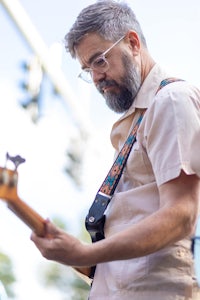 a bearded man with glasses playing a bass guitar